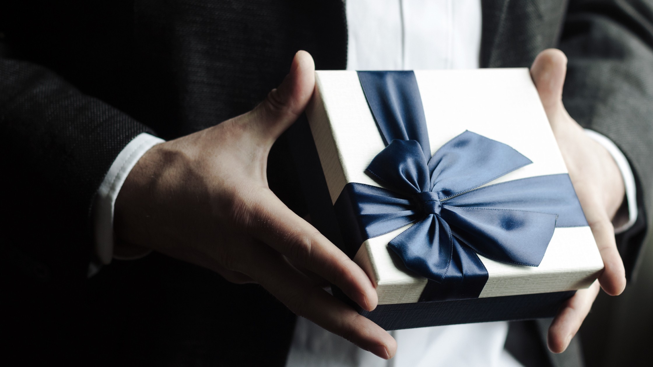 Geschenkbox mit großer Schleife gehalten in Händen 