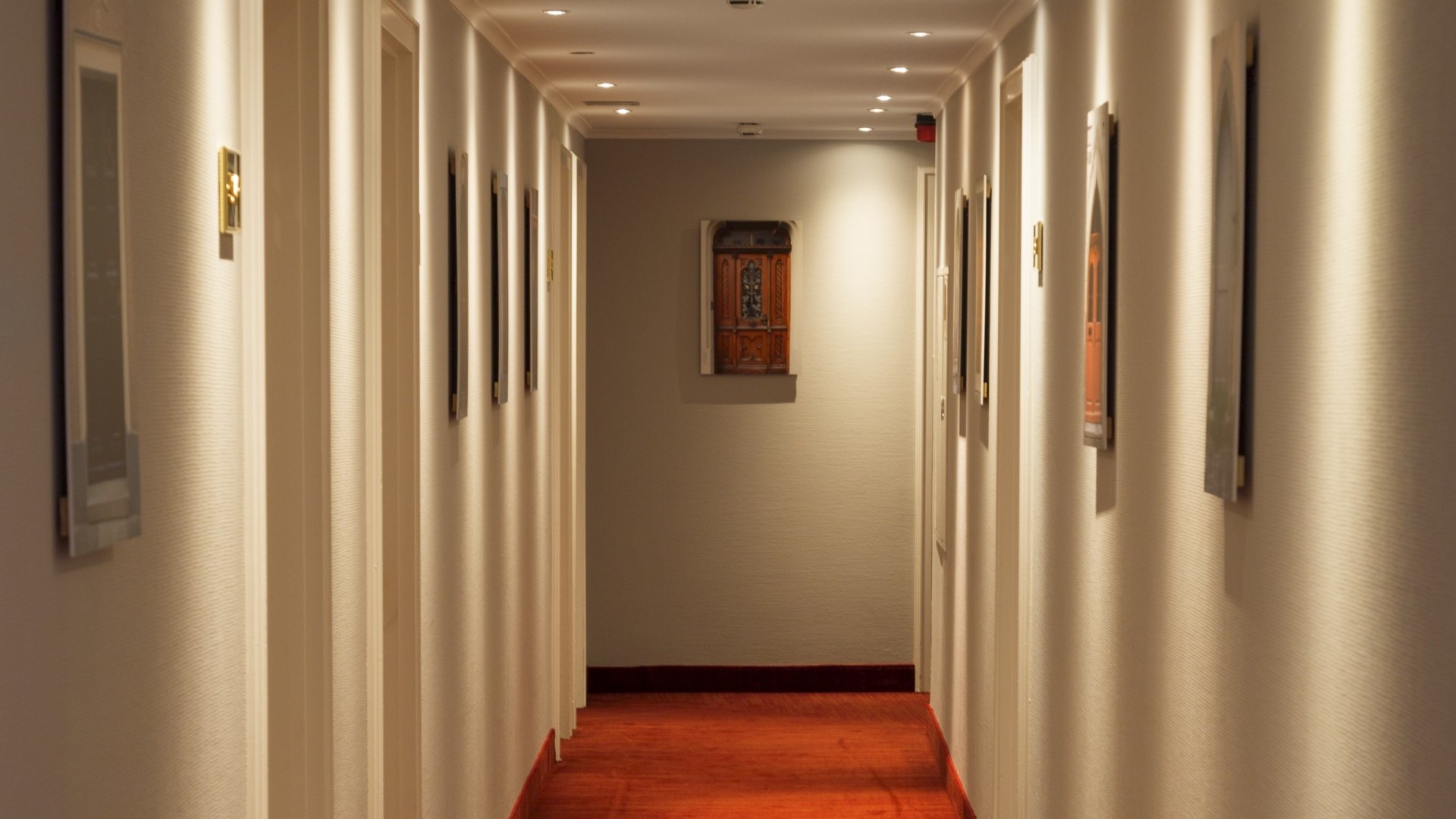  Hotelflur mit Zimmernummerschilder an den Türen und verschiedenen Bildern an den Wänden.