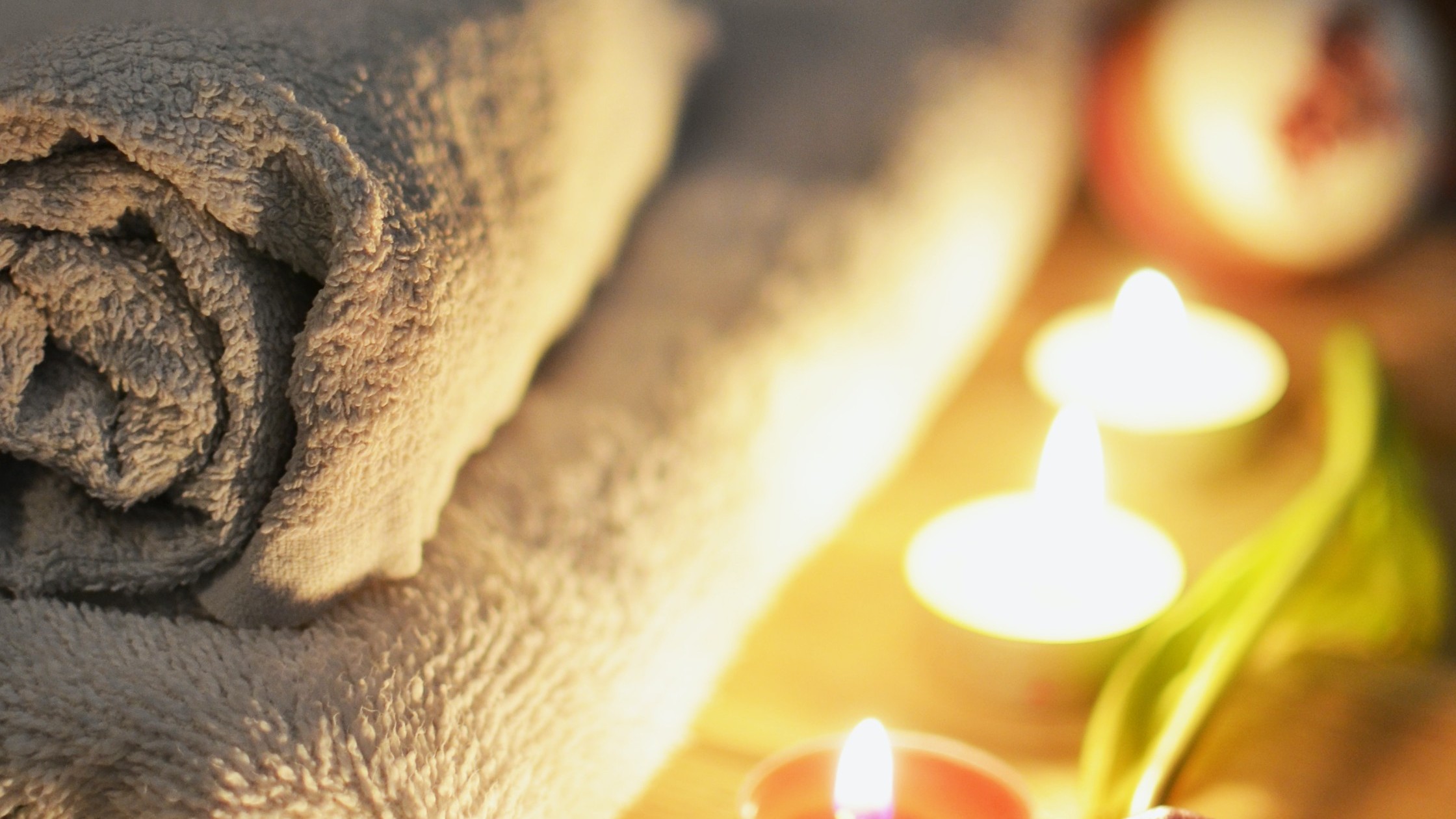 Towels, rolled up on a lounger in the candlelight of colorful candles and a purple tulip.