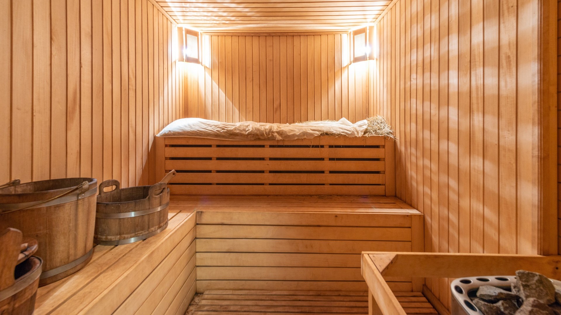 Beleuchtete Holzsauna mit Liegen, Aufgussbehälter und Aufgusssteinen.