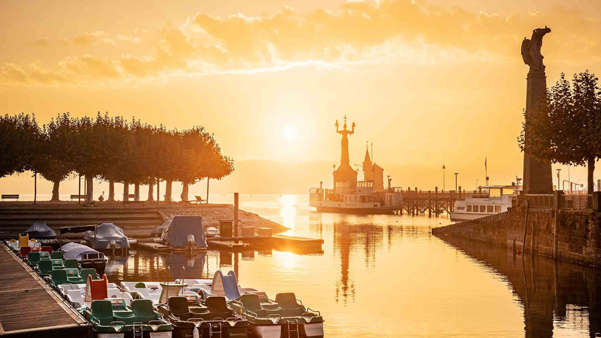 Der Gondelehafen in Konstanz erstrahlt im warmen Licht des Sonnenuntergangs, mit Bootsstegen und dem historischen Konzil im Hintergrund.