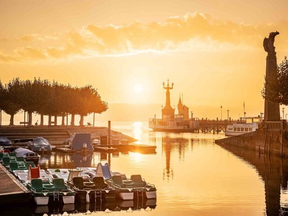 Der Gondelehafen in Konstanz erstrahlt im warmen Licht des Sonnenuntergangs, mit Bootsstegen und dem historischen Konzil im Hintergrund.