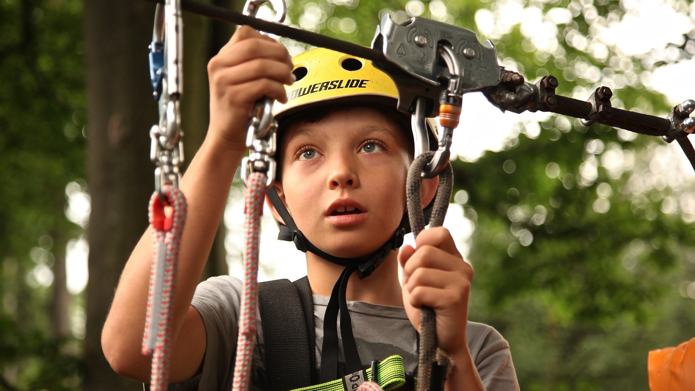 A boy hanging on a climbing wall, looking upwards.