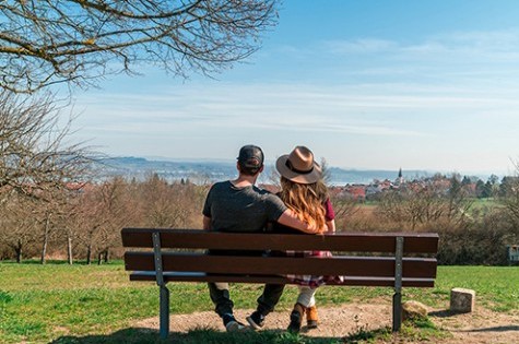Ein Paar sitzt auf einer Bank und blickt entspannt über den Bodensee bei schönem Wetter
