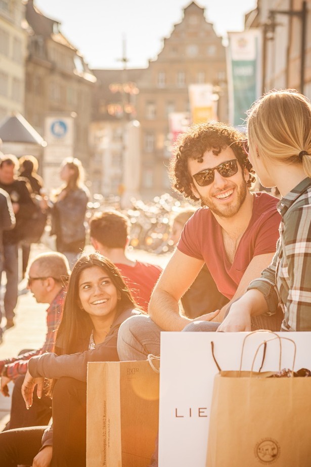 Personen sitzen mit Einkaufstüten in der Konstanzer Innenstadt