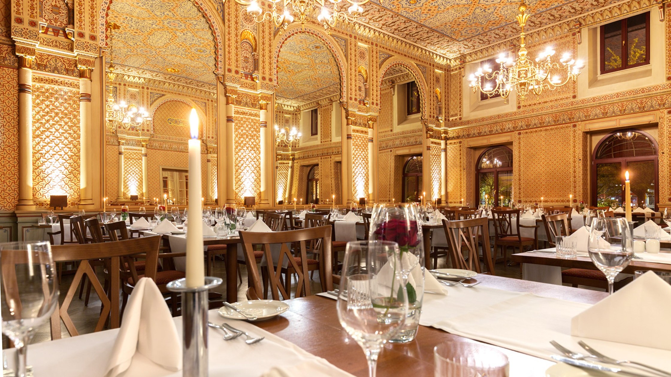 Gedeckte Tische mit roten Rosen und Kerzen im festlichen maurischen Saal, mit Blick auf die gigantischen Spiegeln und die wundervolle Wanddekoration. 