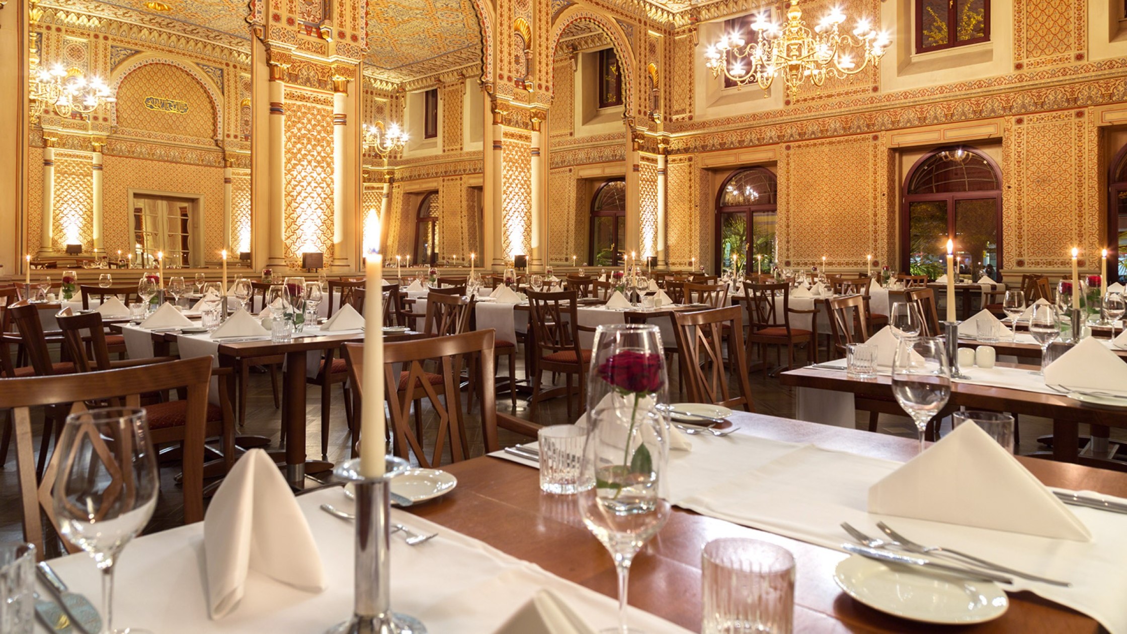  Gedeckte Tische mit roten Rosen und Kerzen im festlichen maurischen Saal, mit Blick auf die gigantischen Spiegeln und die wundervolle Wanddekoration. 