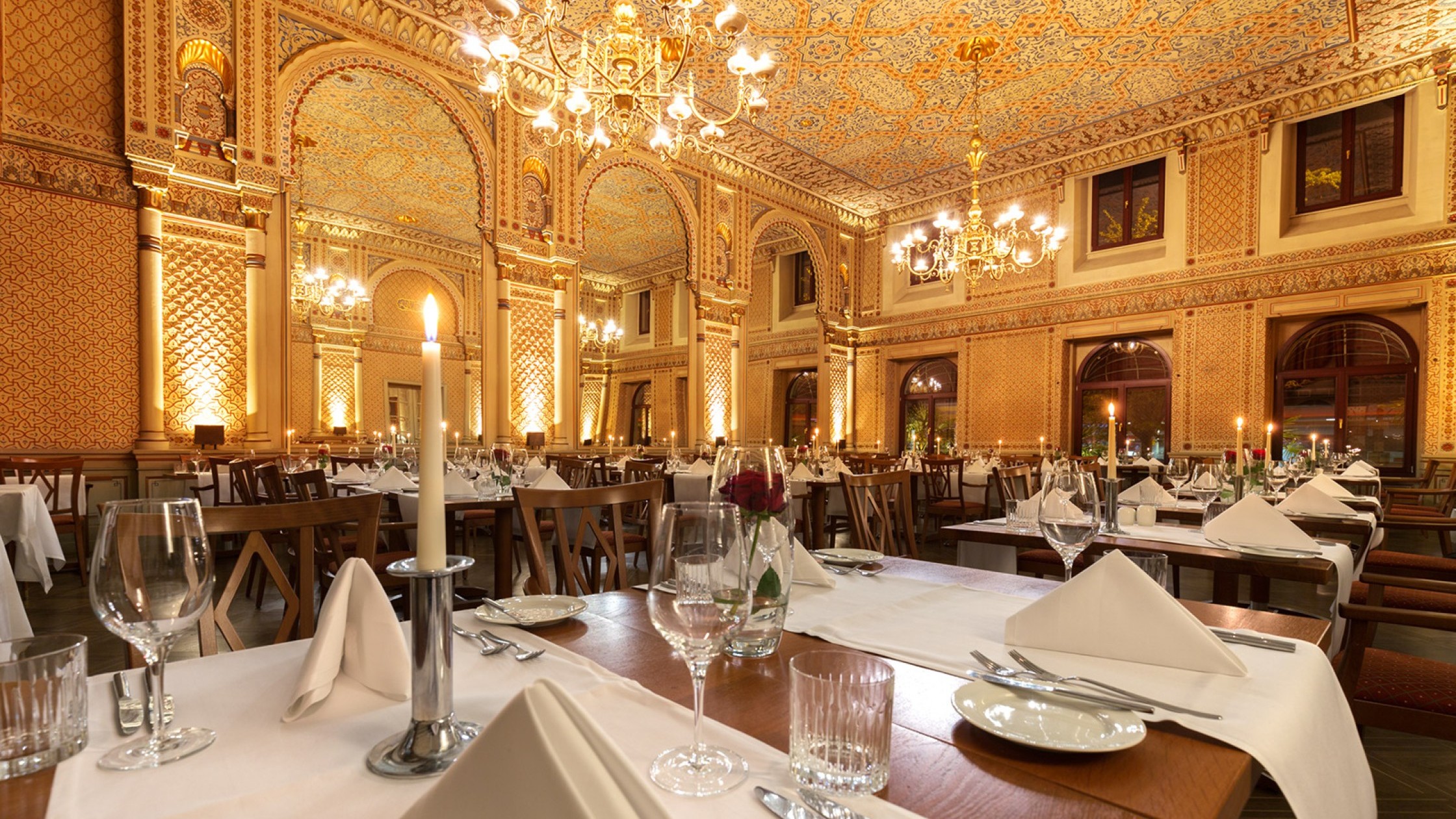  Gedeckte Tische mit roten Rosen und Kerzen im festlichen maurischen Saal, mit Blick auf die gigantischen Spiegeln und die wundervolle Wanddekoration. 