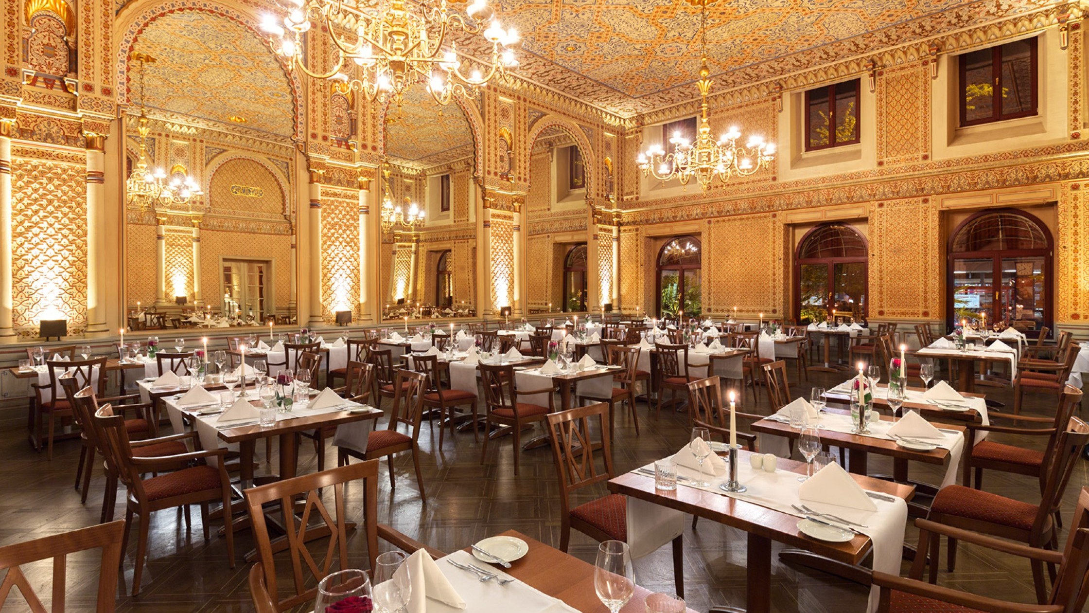  Tables set with red roses and candles in the festive Moorish hall, with a view of the gigantic mirrors and the wonderful wall decorations.