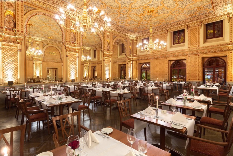 Tables set with red roses and candles in the festive Moorish hall, with a view of the gigantic mirrors and the wonderful wall decorations.