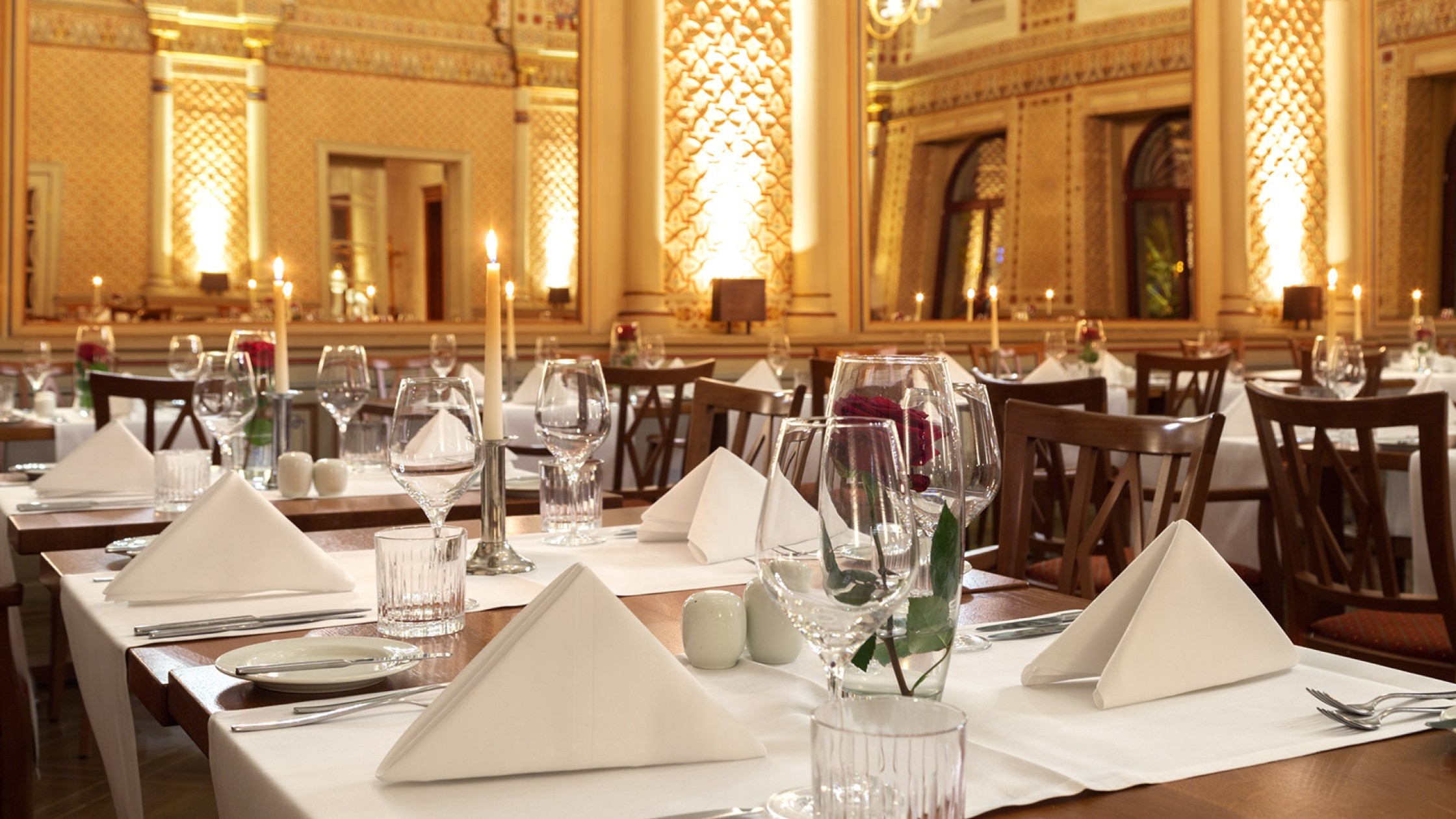  Tables set with red roses and candles in the festive Moorish hall, with a view of the gigantic mirrors and the wonderful wall decorations.