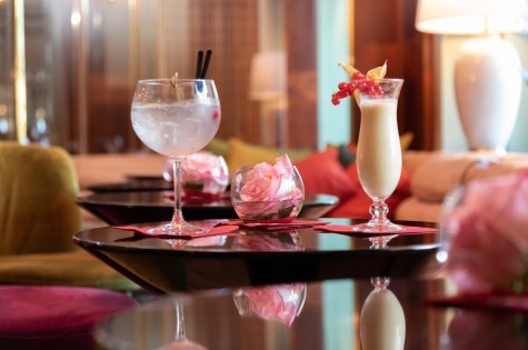 Pina Colada und Gin Tonic auf einem Tisch mit frischer Rose in einer Glasschale in der gemütlichen Hotelbar.