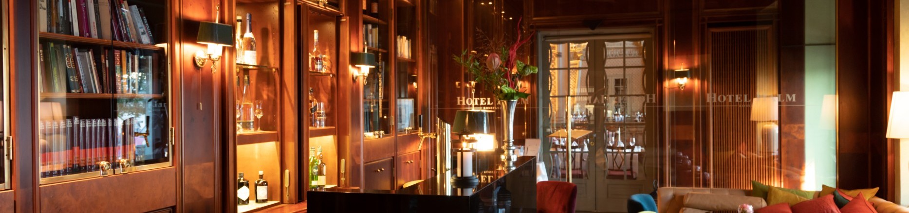  Hotel bar with illuminated shelves full of books, decorated wooden ceiling and cozy seating.