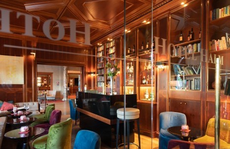 Hotel bar with small tables and cozy loungers, overlooking the entrance area.