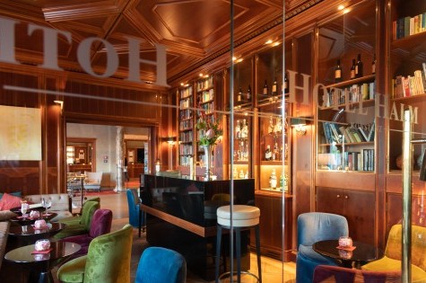 Hotelbar mit kleinen Tischen und gemütlichen Sesseln, mit Blick auf den Eingangsbereich.