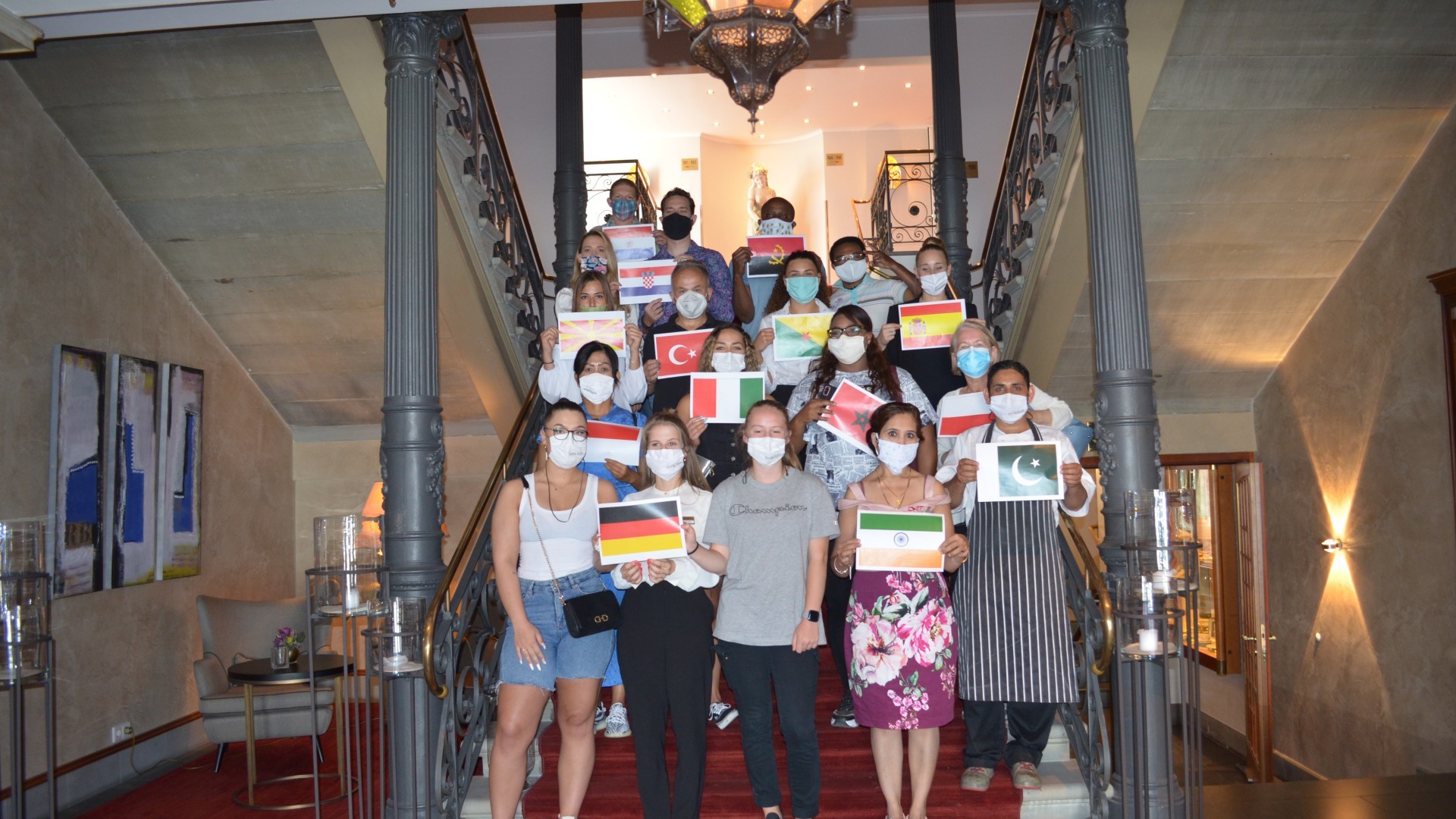Our employees standing on the steps of Hotel Halm, each holding the flag of their country of origin.