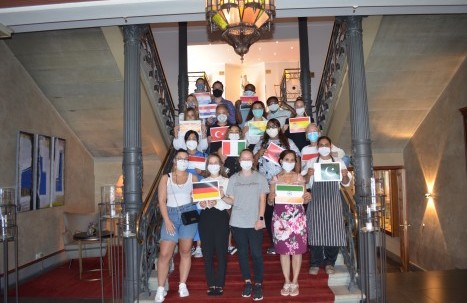 Our employees standing on the steps of Hotel Halm, each holding the flag of their country of origin.