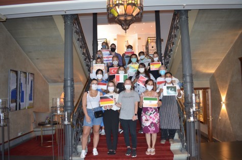 Our employees standing on the steps of Hotel Halm, each holding the flag of their country of origin.